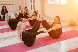 een groep van zes atletisch Dames aan het doen pilates of yoga Aan roze matten in voorkant van een venster in een beige zolder studio interieur. teamwerk, mooi zo humeur en gezond levensstijl concept. foto