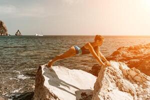 yoga Aan de strand. een gelukkig vrouw mediteren in een yoga houding Aan de strand, omringd door de oceaan en rots bergen, bevorderen een gezond levensstijl buitenshuis in natuur, en inspirerend geschiktheid concept. foto