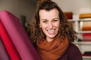vreugdevol jong vrouw Holding levendig kleding stof in creatief werkplaats milieu foto