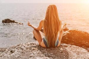 yoga Aan de strand. een gelukkig vrouw mediteren in een yoga houding Aan de strand, omringd door de oceaan en rots bergen, bevorderen een gezond levensstijl buitenshuis in natuur, en inspirerend geschiktheid concept. foto