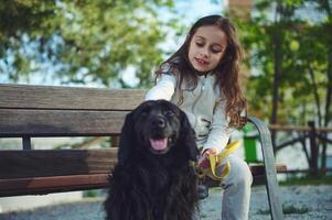 mooi weinig kind meisje 5-7 jaren oud, zittend Aan bank en strelen haar zwart cocker spaniel hond terwijl wandelen het Aan riem. spelen huisdieren. de concept van liefde, zorg en empathie voor huiselijk dieren foto