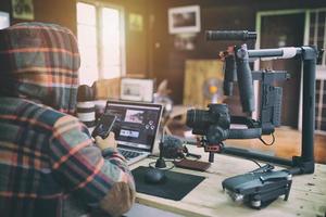 jonge vlogger-man die video op laptop bewerkt en smartphone controleert voor het uploaden van video naar internet online of sociale media. foto