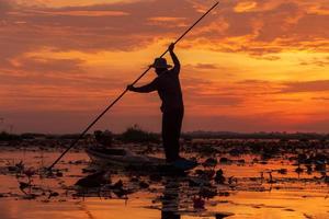 de visser die tijdens zonsopgang aan een boot in het meer werkt, dit is de levensstijl van de visser in udon thani, thailand. foto