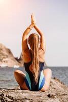 yoga Aan de strand. een gelukkig vrouw mediteren in een yoga houding Aan de strand, omringd door de oceaan en rots bergen, bevorderen een gezond levensstijl buitenshuis in natuur, en inspirerend geschiktheid concept. foto