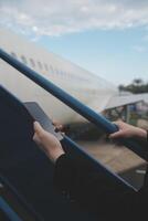 jong Aziatisch vrouw in Internationale luchthaven, gebruik makend van mobiel smartphone en controle vlucht Bij de vlucht informatie bord foto