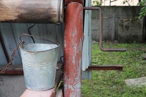 een detailopname van een ijzer aluminium emmer staand in de buurt een rustiek goed Aan een boerderij. apparaat voor extraheren water in landbouw foto