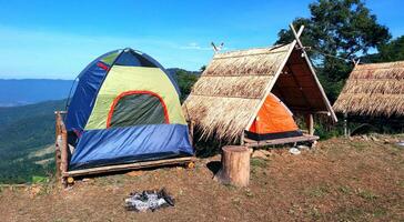 de camping blauw, groen en oranje tent Aan houten afval met droog bladeren dak en blauw lucht, berg en boom voorgrond in zomer tijd. foto