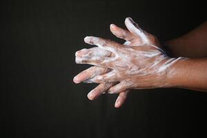 jong Mens het wassen handen met zeep Aan zwart achtergrond foto