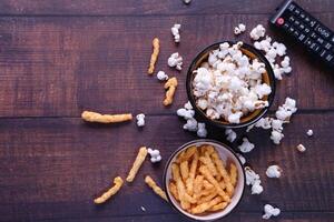 top visie van een kom van popcorn, chips en TV afgelegen Aan houten achtergrond foto