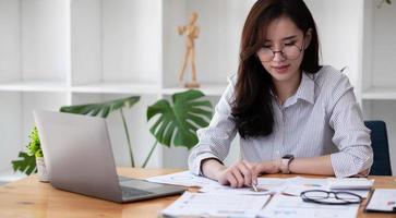 portret Aziatische vrouw met financieel verslag en rekenmachine. vrouw die rekenmachine gebruikt om het rapport aan de tafel op kantoor te berekenen foto