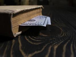 oud boek en tweehonderd dollar bladwijzer in een dik boek. boek op de achtergrond van een houten tafel foto