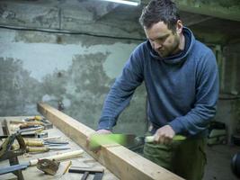 schrijnwerker met een baard die een houten balk zaagt met een handzaag. een timmerman die een stuk hout zaagt foto