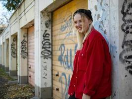 jong meisje in gebreide muts en rode jas glimlachend staande bij de muur met graffiti foto