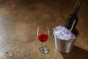 fles rode wijn in een ijsemmer en een glas rode wijn foto