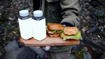 een mannelijke chef-kok die twee hamburgers en twee flessen drankjes bij zich heeft aan de rand van de waterval foto