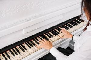 mooie vrouw gekleed in witte jurk spelen op witte piano
