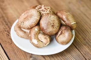 verse champignons op witte plaat en houten tafel achtergrond - shiitake-paddenstoelen foto