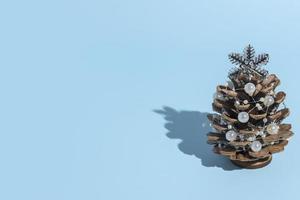 alternatieve kerstboom gemaakt van dennenappels met kralen op een blauwe achtergrond met een harde schaduw met kopieerruimte in een minimalistische stijl voor een nieuwjaarskaart