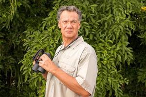 senior man buiten genietend van de natuur kijkend door een verrekijker foto