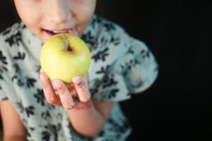 weinig meisje aan het eten appel dichtbij omhoog foto