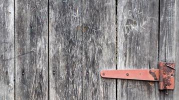oude houten achtergrond met een roestige scharnier. antieke deurscharnieren. rode metalen scharnier op grijs hout close-up gedetailleerde weergave. vintage metalen deur scharnier close-up op oude houten deur achtergrond. foto
