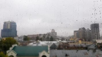 nat raam met druppels op de achtergrond van de herfststad bij bewolkt weer. uitzicht vanuit het raam in de regen. waterdruppel op glazen raam tijdens regen met onscherpe achtergrond van stadsscène foto