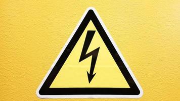 veiligheidsbord geel en zwart gelijmd op een gele muur. hoogspanningsbliksem in een driehoek voorzichtigheid voorzichtigheid gevaar elektriciteit dood. foto