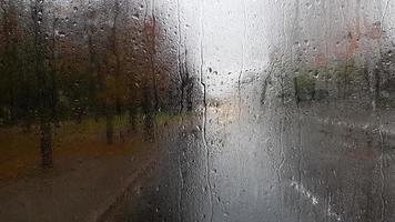 regen op de achterruit van een auto in de herfst. binnenaanzicht van de weg met rijdende auto's in de stad door het raam van de auto met regendruppels. het besturen van een auto in het gezichtsveld van de achterruit. foto