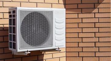 close-up shot van een moderne klimaatbeheersingseenheid tegen de achtergrond van een bakstenen muur van de gevel van een huis buiten. airconditioner aan de muur met ruimte voor tekst. luchtcompressor. foto