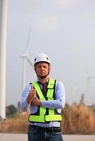 een senior mannetje energie specialist is inspecteren wind turbines Aan een ecologisch bouw project gebruik makend van een wind snelheid meten instrument Bij een windmolen. foto