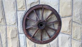oud houten wiel van een kar op een stenen muur van een landelijk huis foto