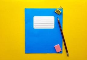 blauwe mock-up notebook en leerboek kont voor schoolvakken, gum, potlood, paperclip op een gele achtergrond. plat leggen, ruimte kopiëren, bovenaanzicht, plaats voor tekst. foto