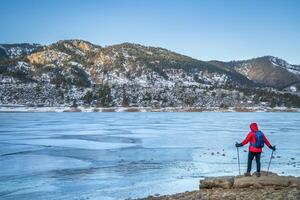 mannetje wandelaar met trekking polen Bij een kust van bevroren paardentand reservoir in de buurt fort collins, Colorado - winter wandelen concept foto