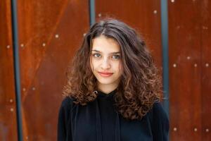 wit brunette tiener- meisje met gekruld haar- poses Aan de straat in de stad. foto