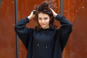 wit brunette tiener- meisje met gekruld haar- poses Aan de straat in de stad. foto