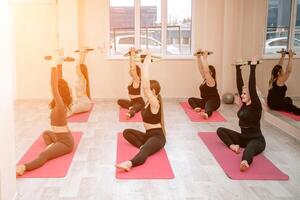 een groep van zes atletisch Dames aan het doen pilates of yoga Aan roze matten in voorkant van een venster in een beige zolder studio interieur. teamwerk, mooi zo humeur en gezond levensstijl concept. foto