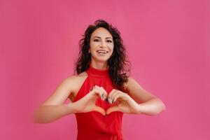 een vrouw in een rood jurk is glimlachen en Holding haar handen samen naar maken een hart vorm geven aan. concept van liefde en geluk. foto