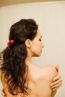 een vrouw met lang haar- is vervelend een rood lint in haar haar. ze is op zoek Bij iets in de spiegel. foto