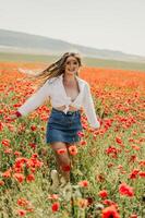 gelukkig vrouw in een papaver veld- in een wit overhemd en denim rok met een krans van klaprozen Aan haar hoofd poseren en genieten van de papaver veld. foto