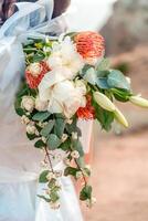 een vrouw is Holding een boeket van bloemen, met een wit jurk en een boog. de bloemen zijn een mengen van rood en wit. foto