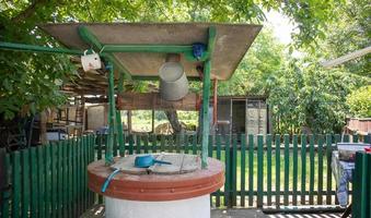 een oude waterput met een emmer in de tuin, een metalen handvat om water uit de grond te halen. dorp goed onder het dak met een touw. retro goed op het platteland. foto