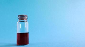 een glazen transparante fles met rood medicijn voor vaccins op een blauwe achtergrond op een medisch thema met kopieerruimte. medische vaccinatie tegen het concept van coronavirus griep. foto