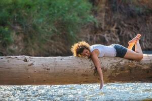 gelukkig jong vrouw poseren Aan een log over- een rivier- foto