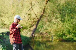 Mens ontspannende en visvangst door oever van het meer. weekends gemaakt voor vissen. visser mannelijk hobby. meester lokaas. houden kalmte en vis Aan. fishman gehaakt spinnen in de rivier- aan het wachten groot vis. vent vlieg visvangst foto