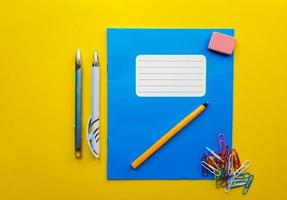 blauwe mock-up notebook en leerboek kont voor schoolvakken, gum, potlood, paperclip op een gele achtergrond. plat leggen, ruimte kopiëren, bovenaanzicht, plaats voor tekst. foto