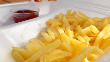 een close-up van goudoranje gele frietjes met tomatenketchup geserveerd in een schuimcontainer. fastfood afhaalmaaltijden. ongewenst vers voedsel. foto