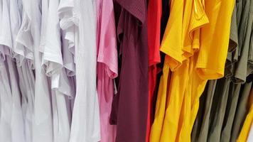 kleuren van de regenboog. verscheidenheid aan casual shirts, t-shirts op hangers in een winkel. doek katoen van verschillende felle kleuren close-up. textiel achtergrond foto