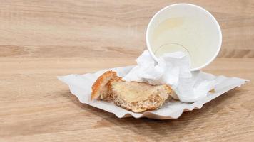 overgebleven voedsel op een papieren bord en lege vuile papieren koffiekop op een houten tafel in een fastfoodcafé foto