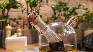 glazen fles met saus en boter voor pizza en pasta, staande op een geserveerd houten tafel in een italiaans restaurant met bakstenen muren en groene planten. foto