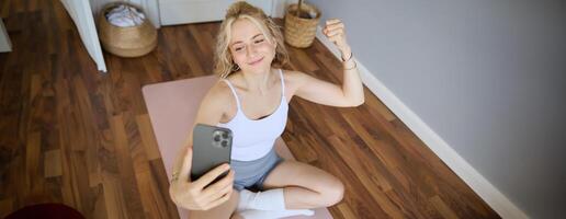 portret van jong sportief vrouw nemen selfie gedurende training opleiding, inhoud Schepper duurt foto's, shows spieren Aan camera, buigen biceps foto